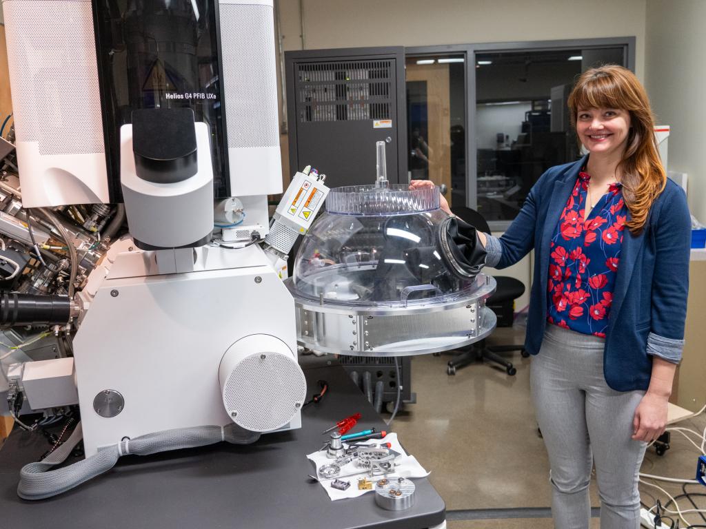 Valerie Brogden poses next to the the Noble Dome, a transparent dome with gloves attached, connected directly to a microscope.