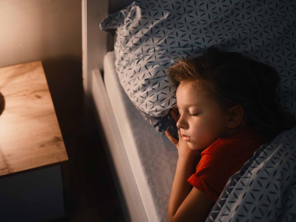 A young child sleeping in bed with their head on a pillow.