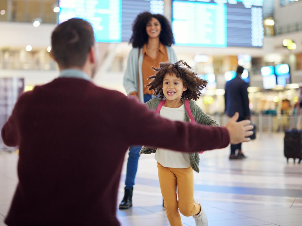 A happy young child running through an airport toward a person with their arms outstretched for a hug.