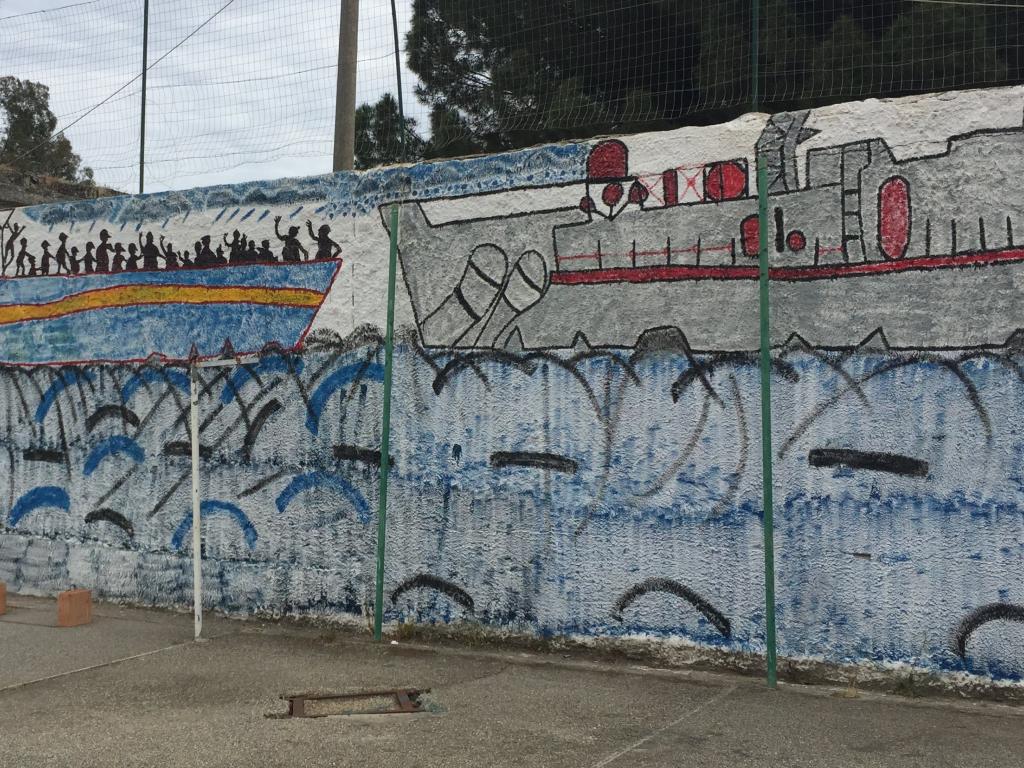 A mural of migrants on a boat painted on a wall.