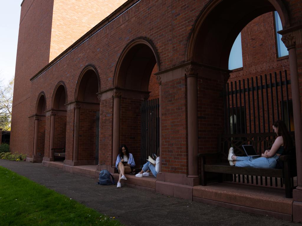 Three students sit and study outside the Jordan Schnitzer Museum of Art on a sunny day.