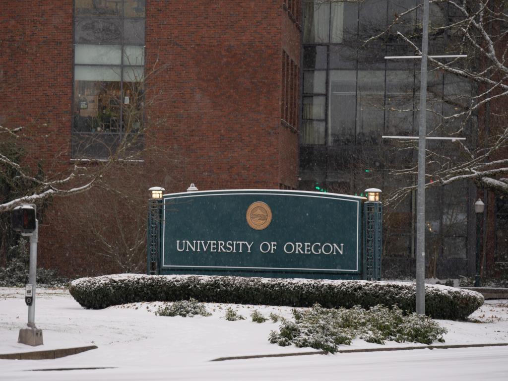 A light layer of snow blankets a sign reading University of Oregon.