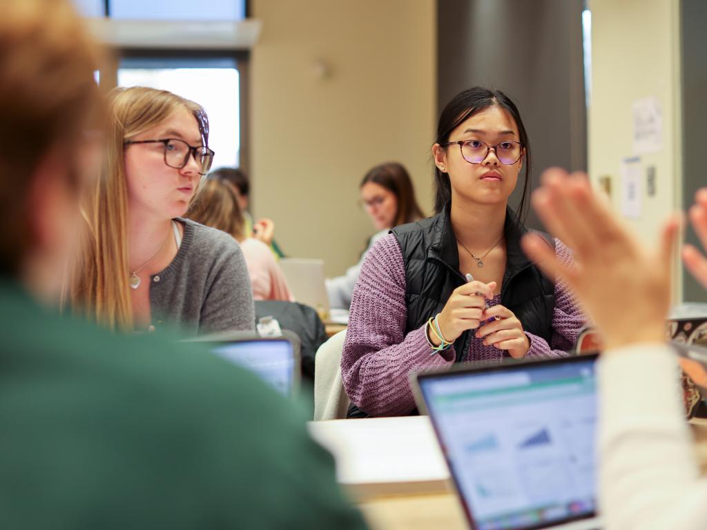 Four people sitting at a table have a discussion with computers open before them.