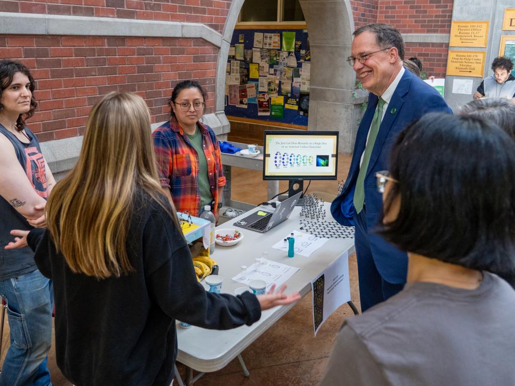 Students stand around a table in conversation with UO president John Karl Scholz.