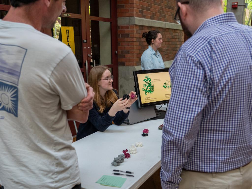 A person sitting at a table holds 3d printed objects in her hands while talking to people standing around the table.