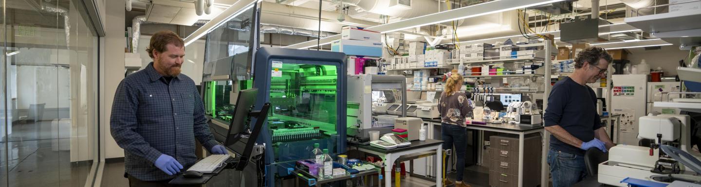 Three people stand in a lab, each working on a different instrument.