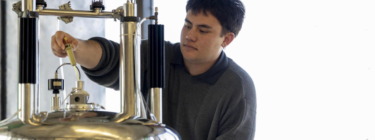 A student reaches out to load a sample into the top of a spectrometer.