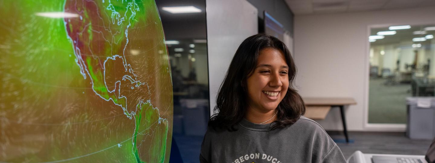 A student laughs while standing in front of a large screen in the Dream Lab.