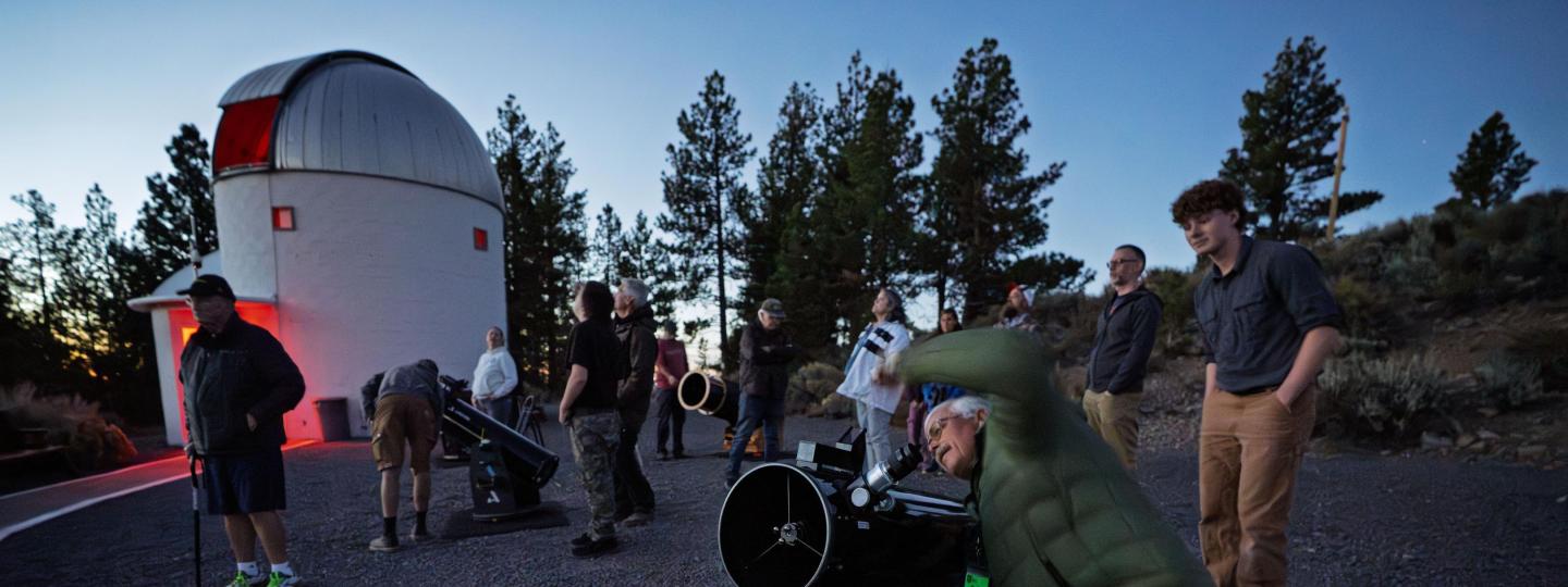 A group of people take turns looking through telescopes outside of the Pine Mountain Oversavatory.
