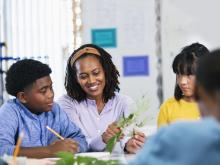 An educator and a child in a classroom examine leaves.