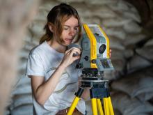 A student uses a surveying instrument in a rockshelter cave.