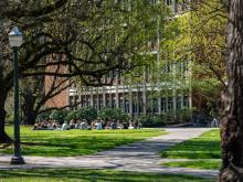 Students sit in a circle outside of a brick campus building on a spring day.