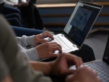 A person sits with a laptop on their lap.