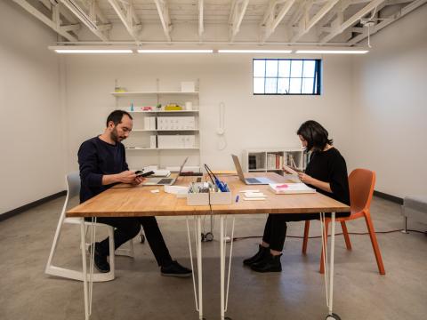 Two people sit at a table using computers