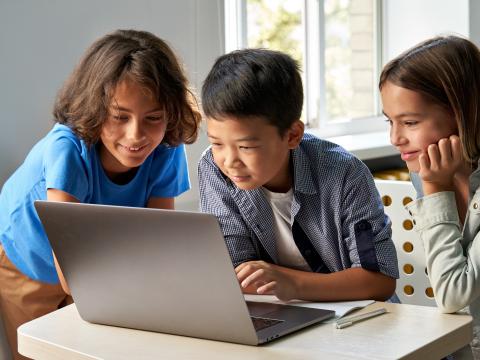 Three children look at laptop screen.
