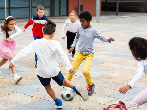 A group of six children play soccer together in a paved courtyard.
