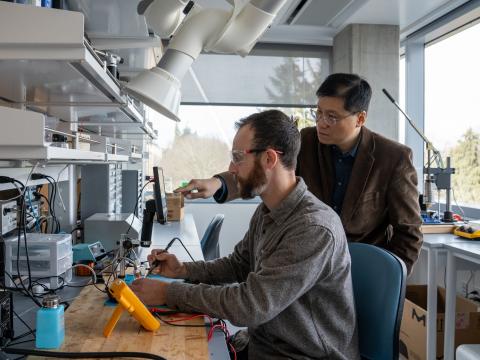 Professor Keat Ghee Ong points at a computer screen while a lab assistant holds a sensor.