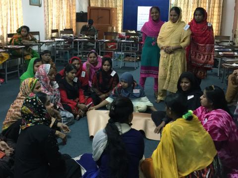 Women gather both sitting and standing in a circle in a classroom.