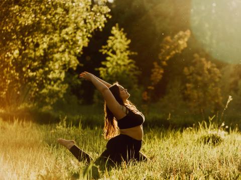 A woman stretches in a yoga pose in a sunny, grassy field. 