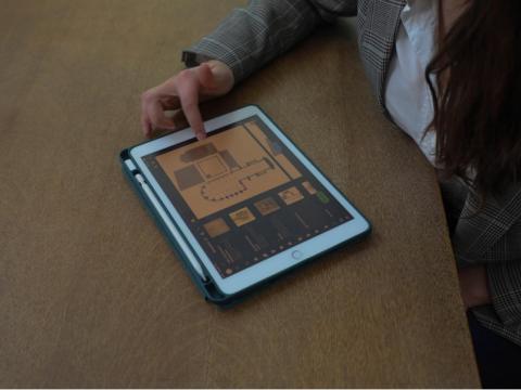  Gabriela Chitwood touching the screen of an Ipad where there is the floor plan of the Toulouse Cathedral and all the different plans of the Cathedral, she’s sitting in a chair and the Ipad is on the table. 