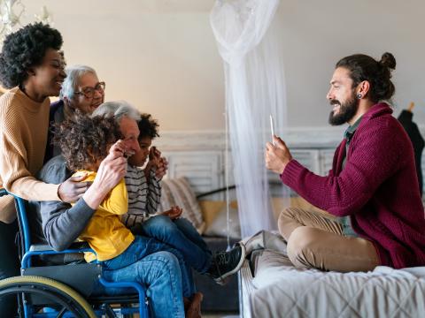 A person sitting on a bed takes a photo of a group of smiling kids and adults.