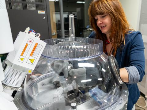 A scientist transfers a sample in a clear, dome-shaped vacuum chamber attached to a microscope.
