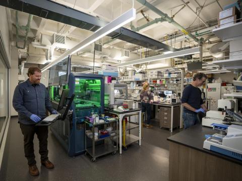 Three people stand in a lab, each working on a different instrument.