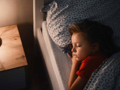 A young child sleeping in bed with their head on a pillow.