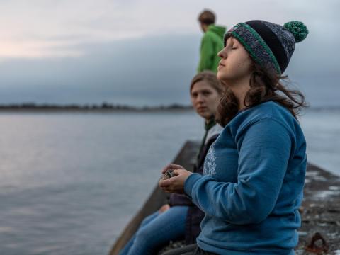 A student standing on a dock closes her eyes and turns her head toward the setting sun.