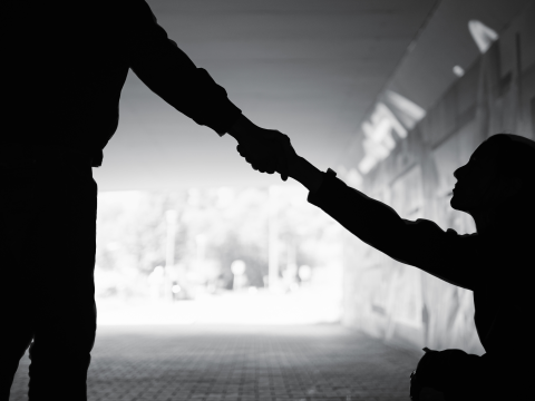 Silhouette of a person extending a hand to help someone up.