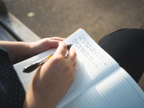 A person sits with a notebook in their lap and a pen in their hand.