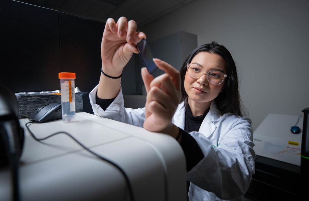 Young woman with glasses holds up test tube in lab