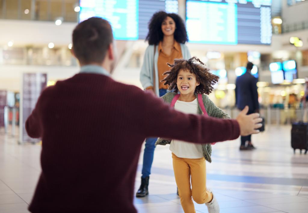 A happy young child running through an airport toward a person with their arms outstretched for a hug.