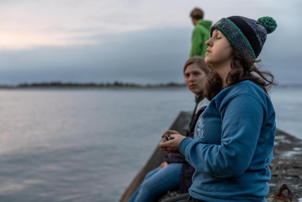 A student standing on a dock closes her eyes and turns her head toward the setting sun.