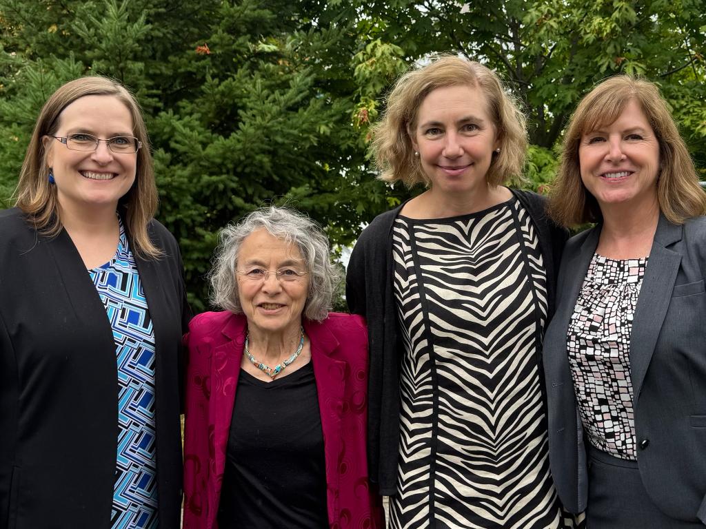 Four women stand closely together and smile.