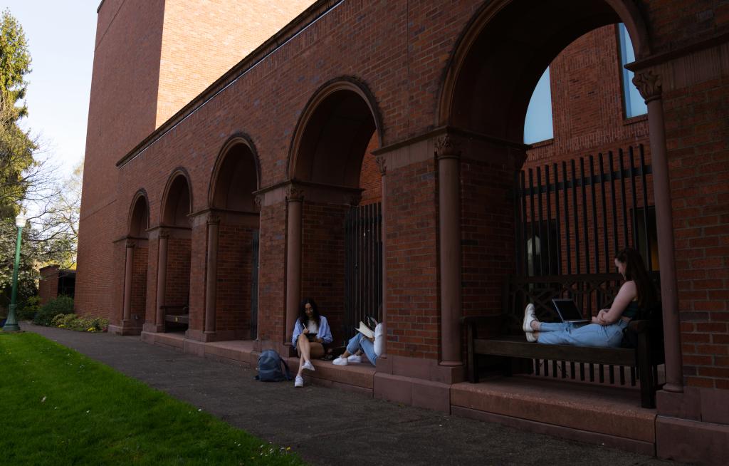 Three students sit and study outside the Jordan Schnitzer Museum of Art on a sunny day.
