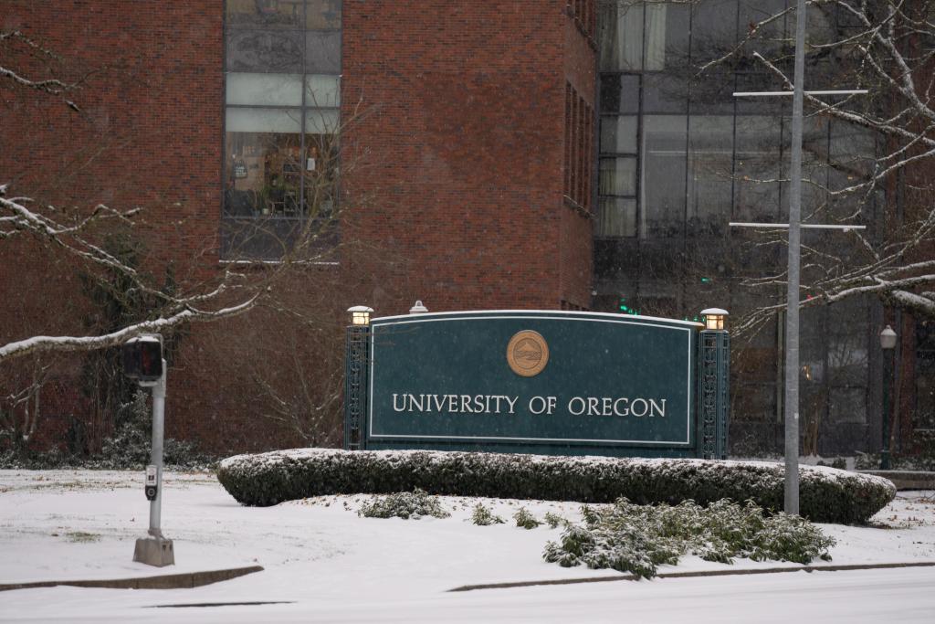 A light layer of snow blankets a sign reading University of Oregon.