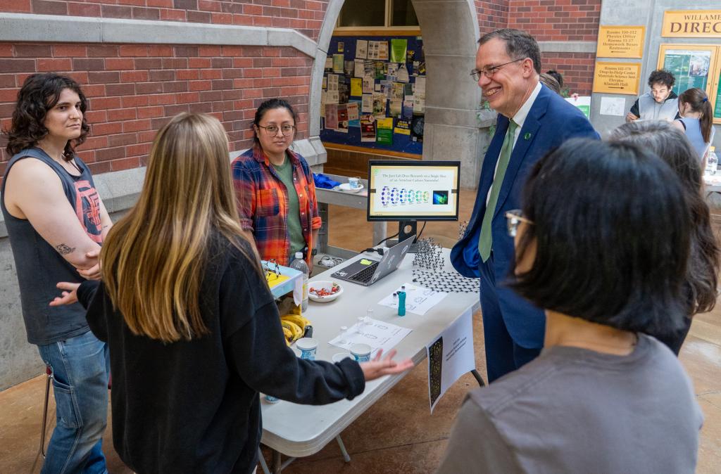Students stand around a table in conversation with UO president John Karl Scholz.