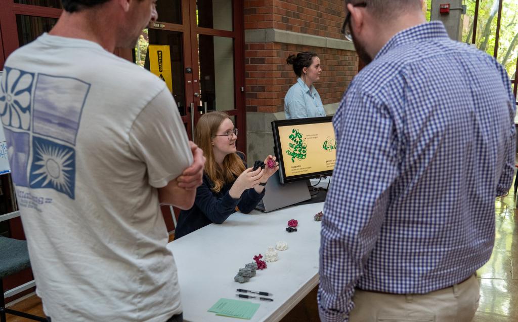 A person sitting at a table holds 3d printed objects in her hands while talking to people standing around the table.