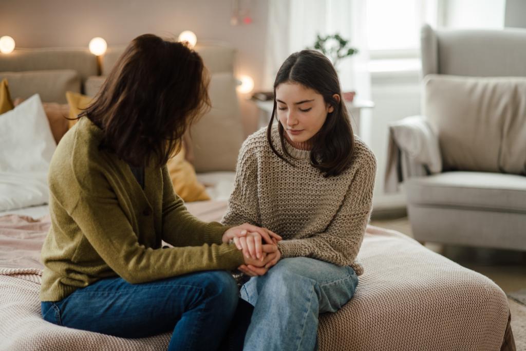 A mother sits on the edge of a bed, comforting her daughter.