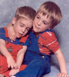 A young boy has his arm over another young boys shoulder as they pose for a picture.