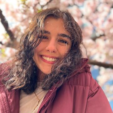 A portrait of Ava Minu-Sepehr in front of a blossoming tree.