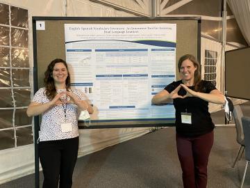 De Anda and Cycyk stand in front of a research poster while holding their hands in the “Throw the O” gesture that creates an O with the fingers.