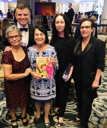 Ernesto Martínez standing next to Adelina Anthony and Dolores Huerta holding children’s book. 