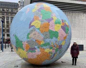 A person stands on a street next to a globe that is roughly twice the size of the person.
