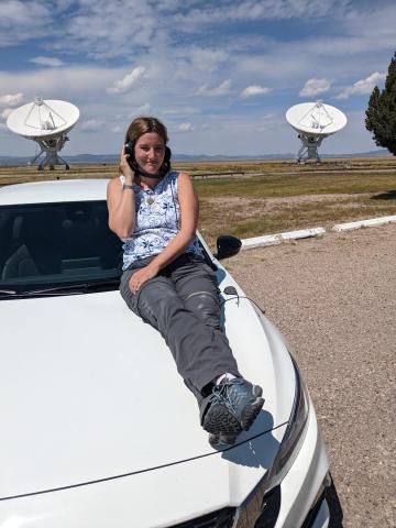 Yvette Cendes poses in front of two radio telescopes. 