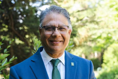 Man in suit and tie with glasses smiled in front of trees