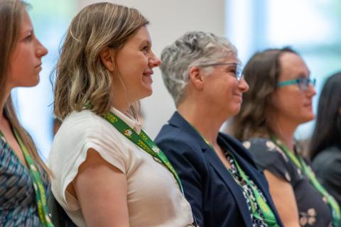 Four women seen from the side look in the same direction at a person speaking, who is not visible in the photo.