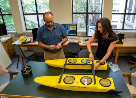 Two people assemble a small catamaran-type research drone in a lab.