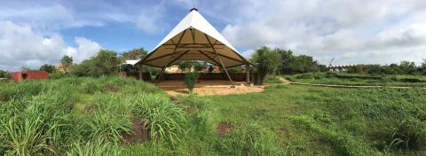 A large canvas canopy covers a dirt area in a field of green grasses.